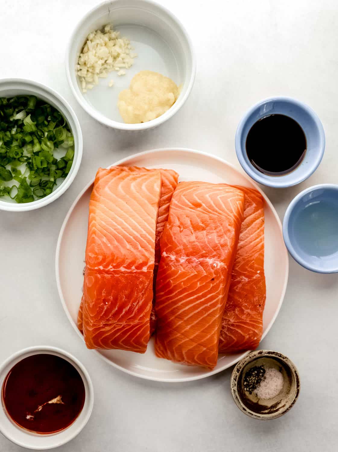 Overhead view of ingredients needed to make salmon in separate bowls on white surface. 
