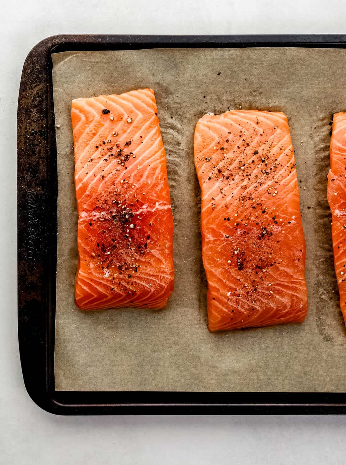 Salt and pepper seasoned salmon on parchment lined baking sheet. 