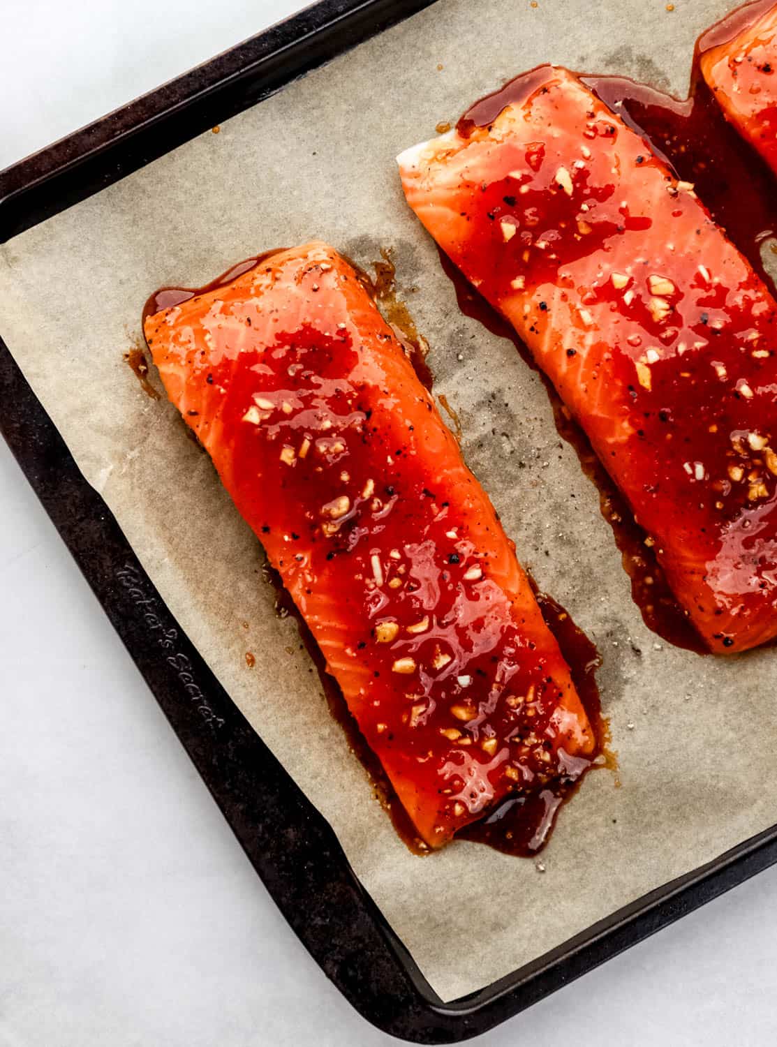 Overhead view of unbaked glazed salmon on parchment lined baking sheet. 