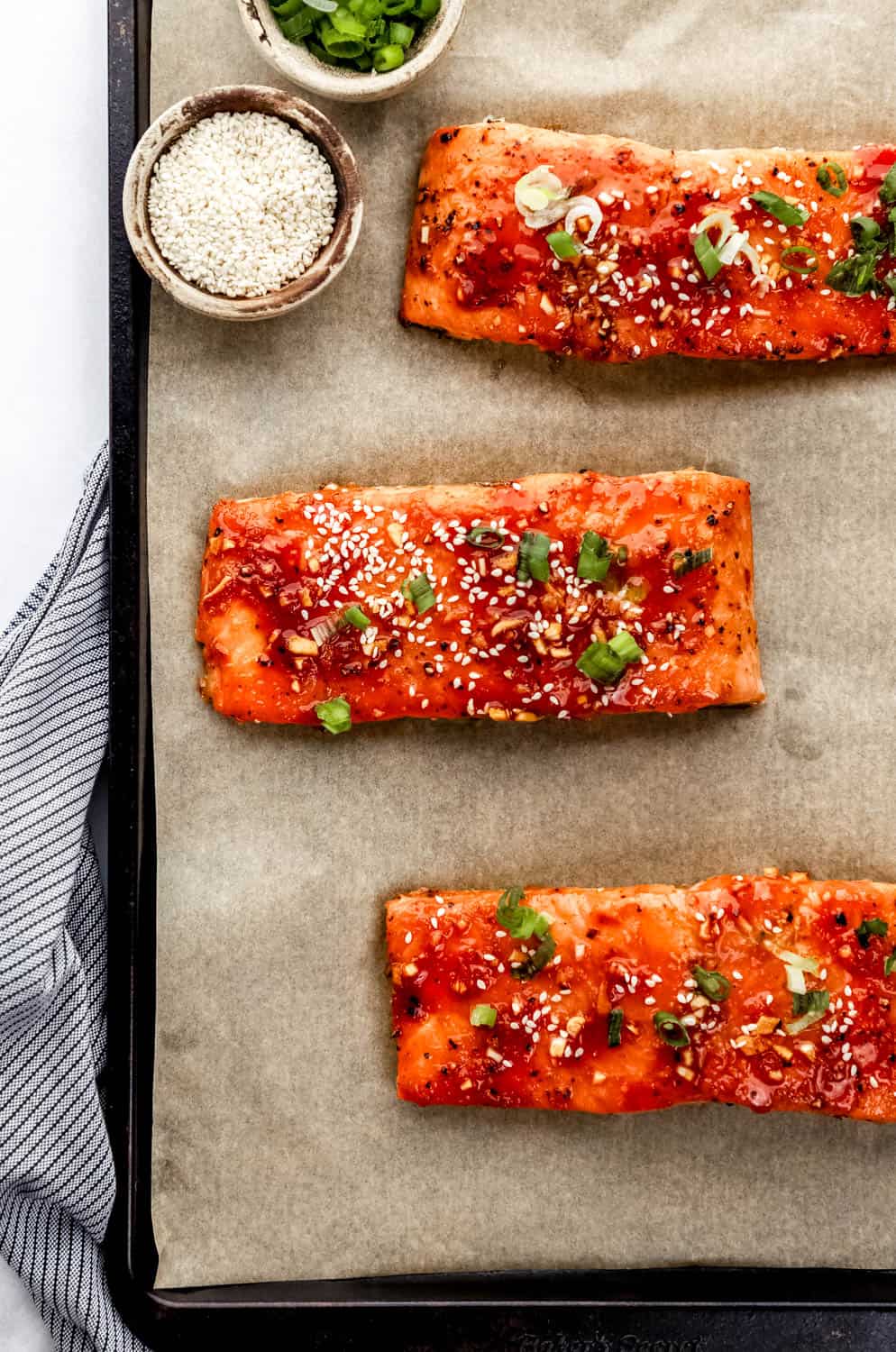 Overhead view of finished salmon on parchment lined baking sheet topped with sesame seeds and green onion. 