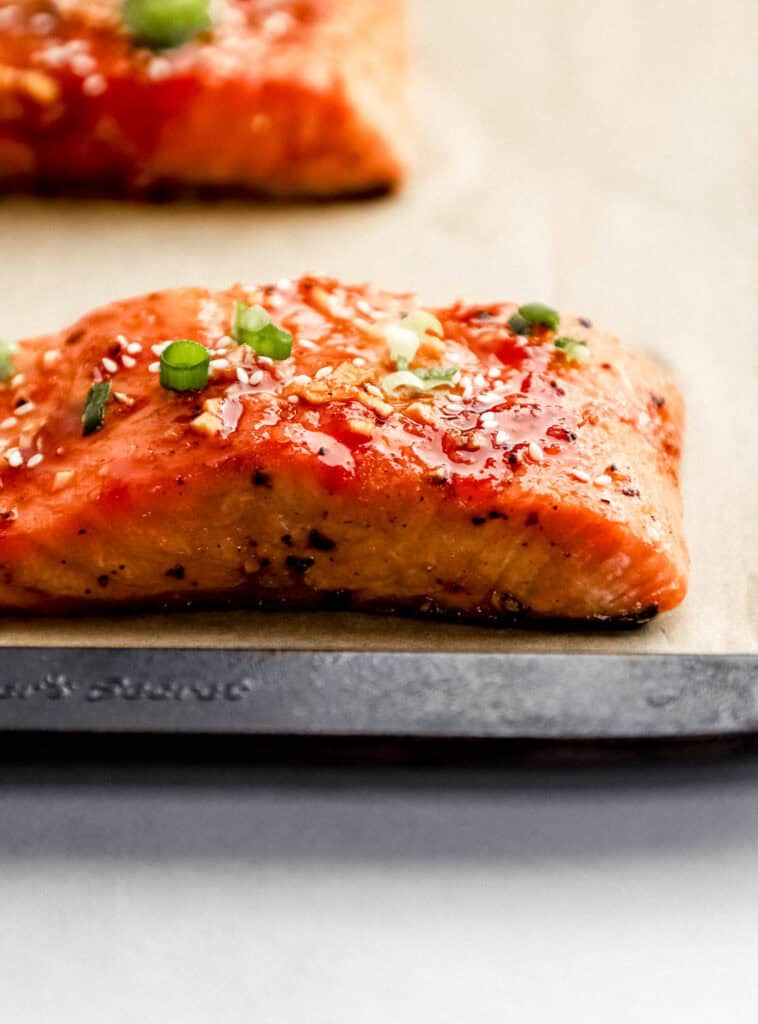Close up side view of finished salmon on parchment lined baking sheet topped with sesame seeds and green onion.