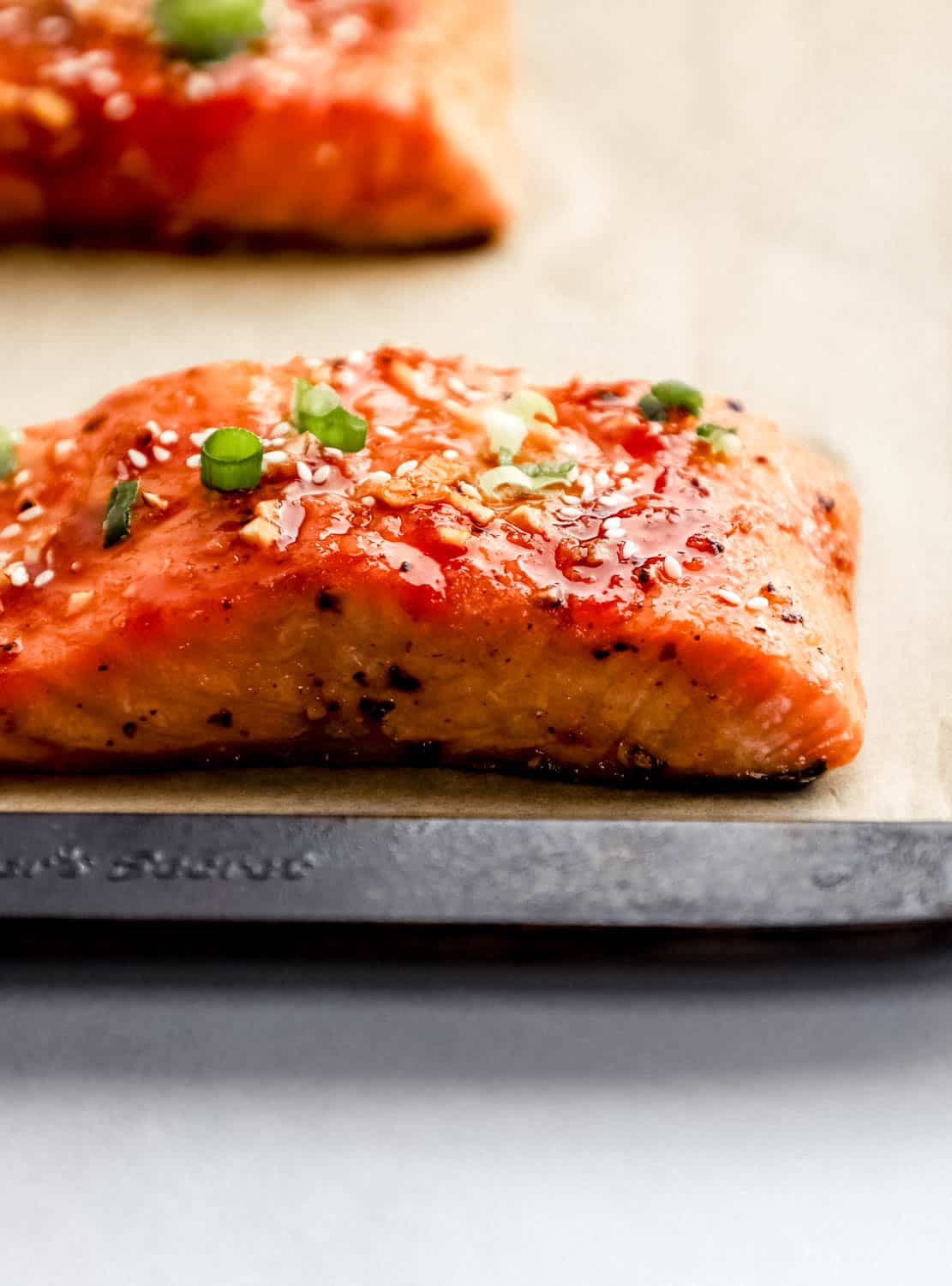 Close up side view of baked salmon on parchment lined baking sheet topped with sesame seeds and green onion. 
