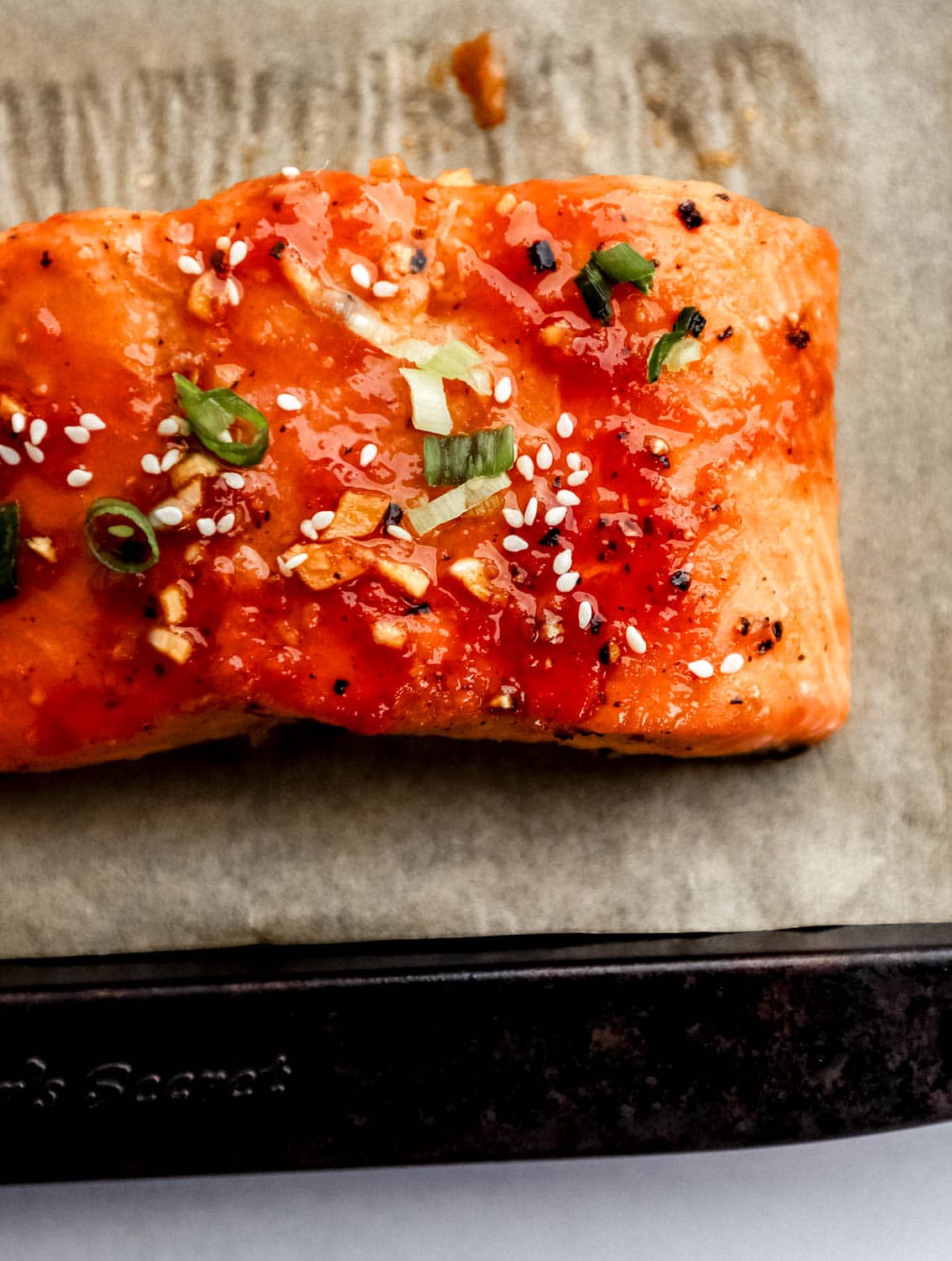 Close up view of piece of salmon on parchment lined sheet pan. 