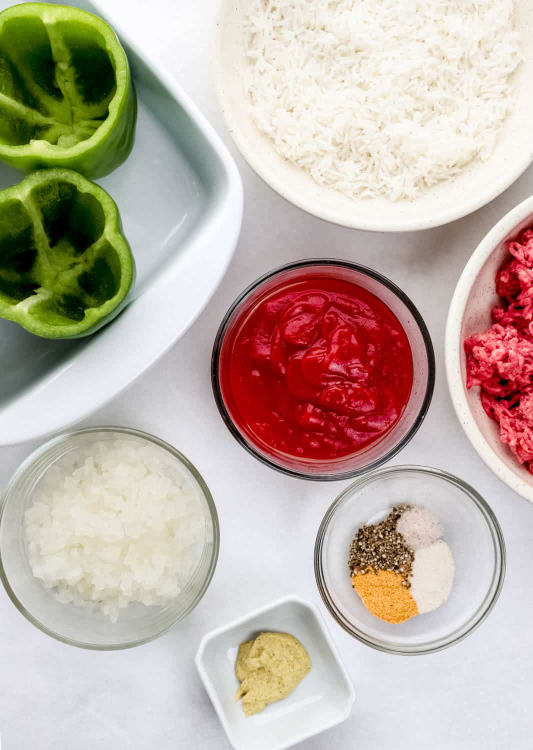 Overhead view of ingredients needed to make stuffed peppers in separate bowls on white surface. 