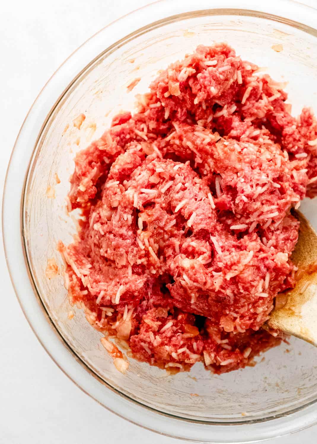 Meat mixture in large glass mixing bowl with wooden spoon. 