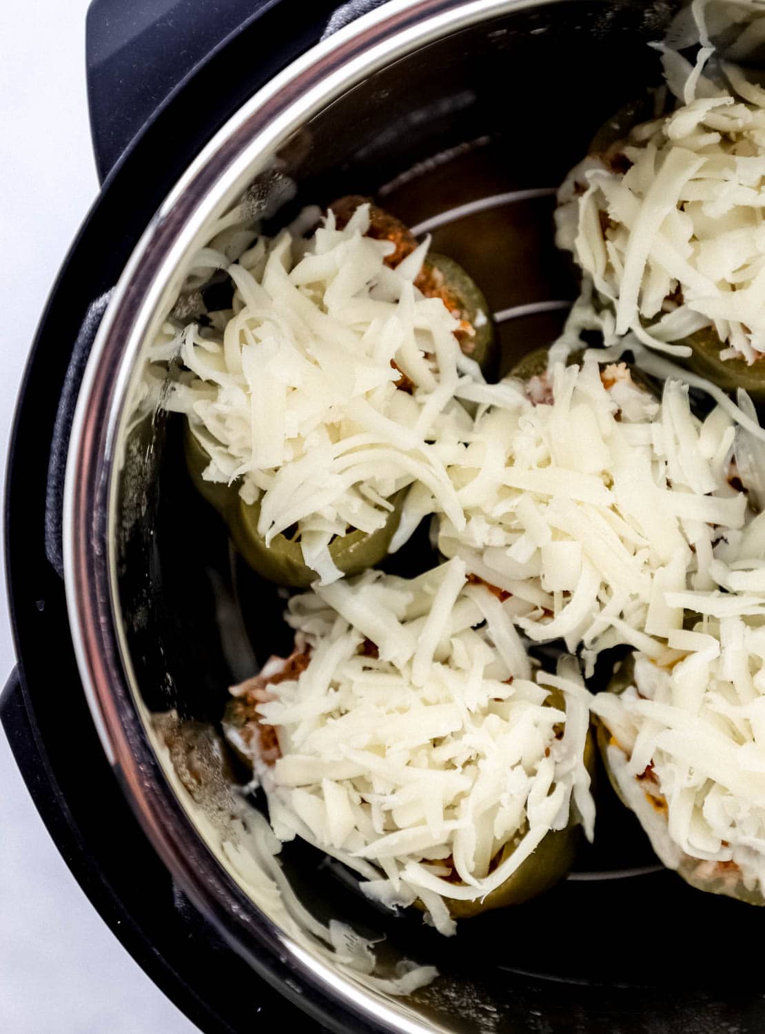 Overhead view of cooked peppers topped with shredded cheese in instant pot. 