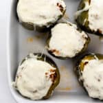 Overhead view of finished stuffed peppers topped with melted cheese in white baking dish.