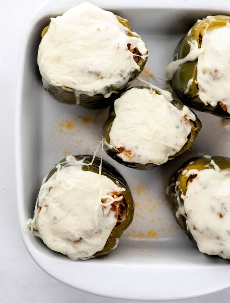 Overhead view of finished stuffed peppers topped with melted cheese in white baking dish.