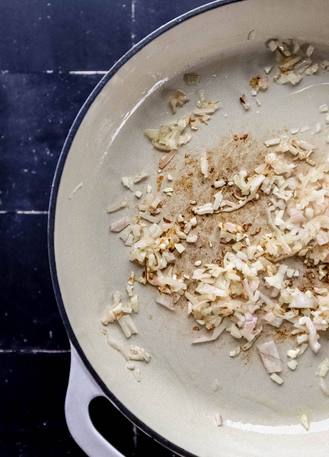 Overhead view of shallot and garlic in braiser pan. 