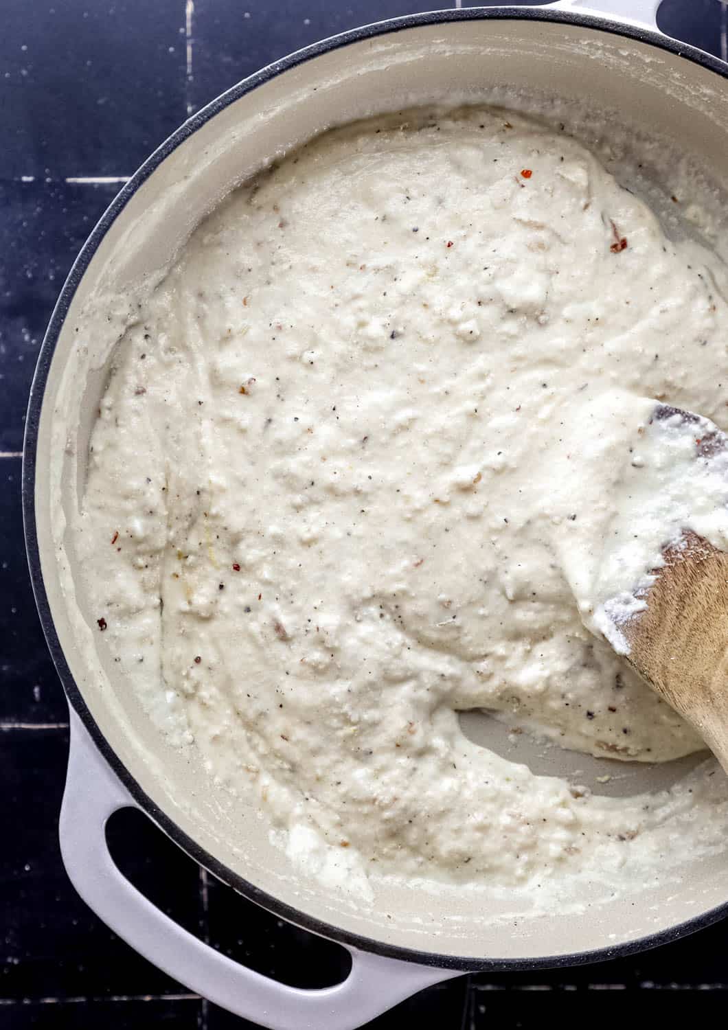 Ricotta sauce in large white braiser with wooden spoon. 