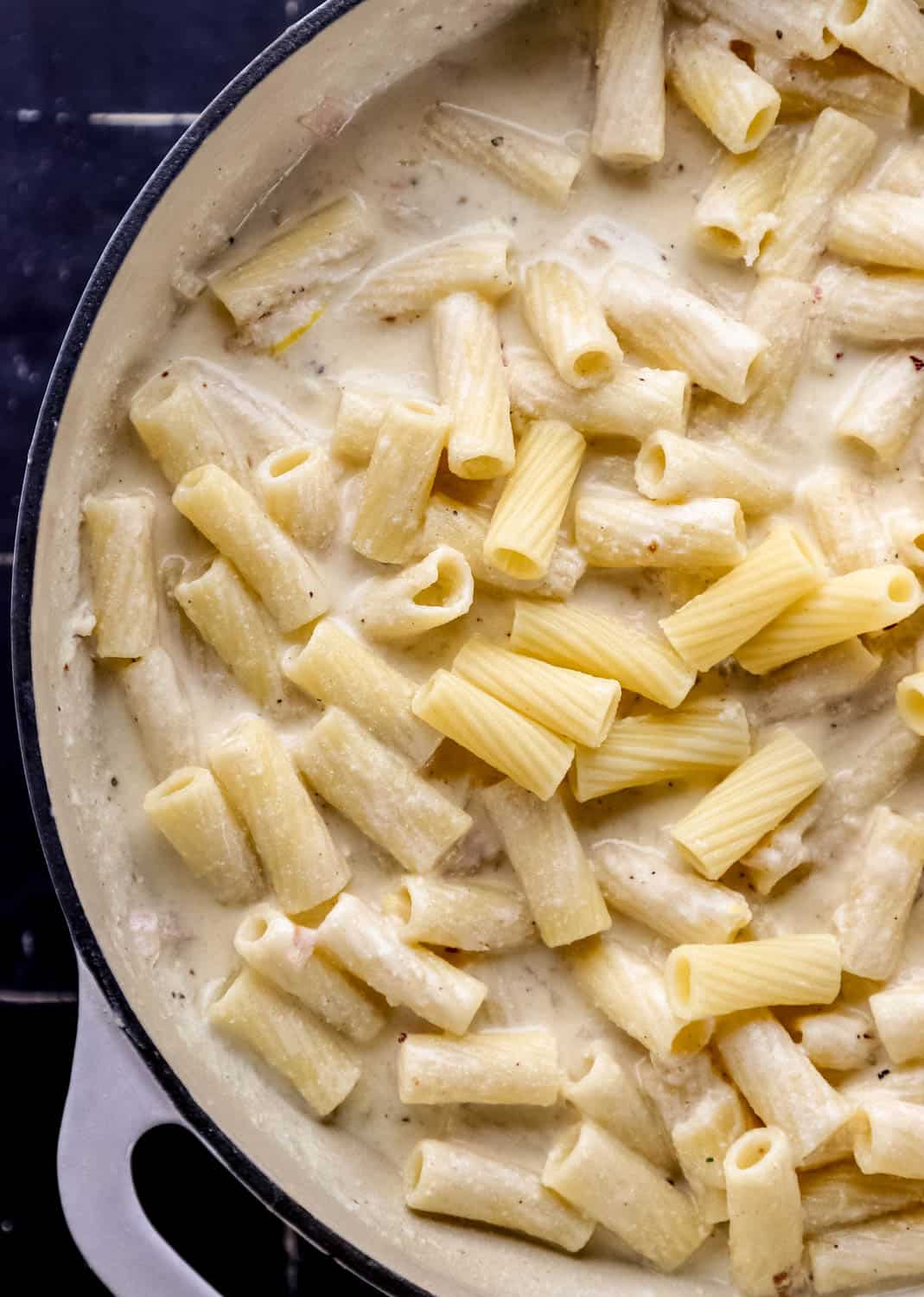 Cooked pasta added to ricotta sauce in large white braiser. 