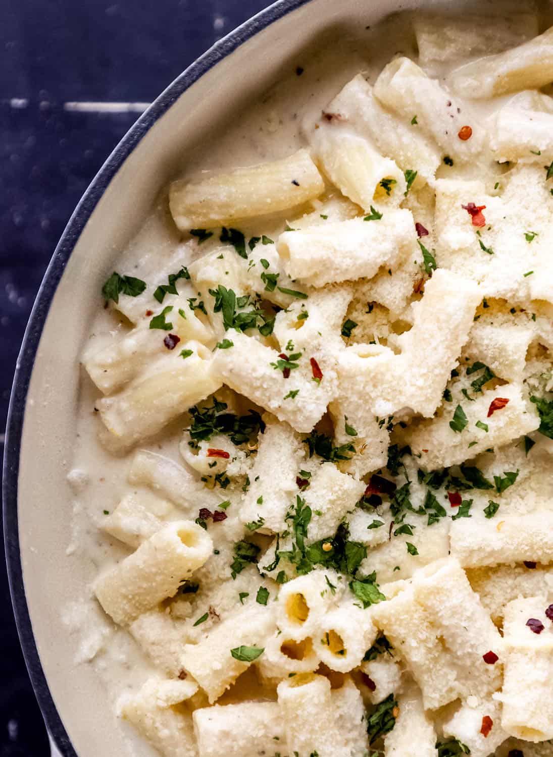 Close up view of finished ricotta pasta in large white braiser topped with parsley, parmesan, and red pepper. 