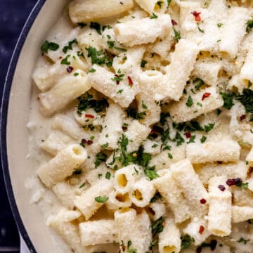 Overhead view of pasta with ricotta and lemon in large white braiser pan on black tile surface.