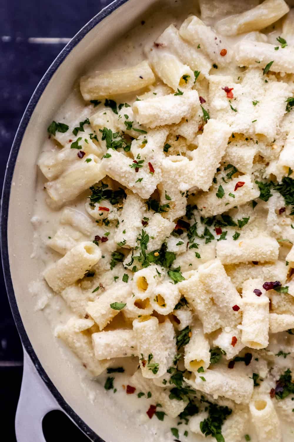 Overhead view of lemon ricotta pasta in white braiser topped with chopped parsley, crushed red pepper, and grated parmesan.