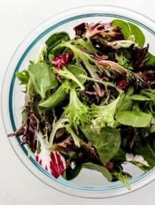 Overhead view of mixed salad green in large glass mixing bowl.