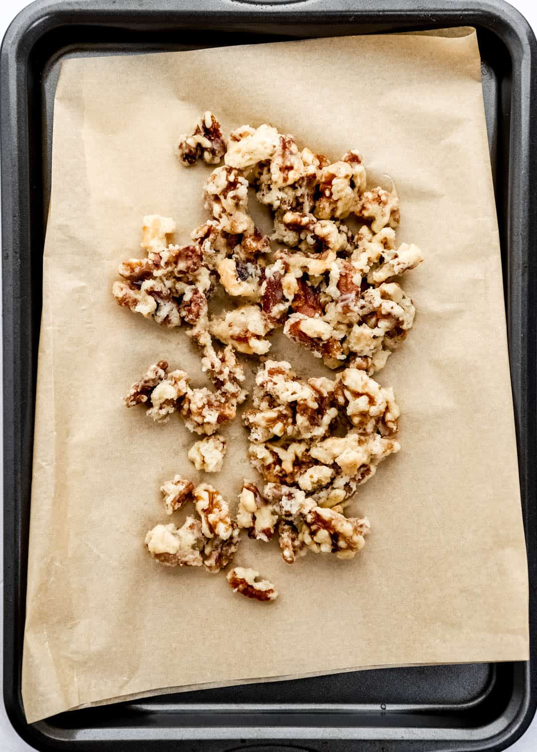 Overhead view of parchment lined baking sheet with candied walnuts on it. 