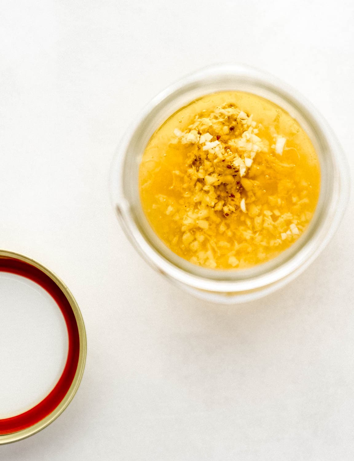 Jar with dressing ingredients combined in it by the lid on white surface. 