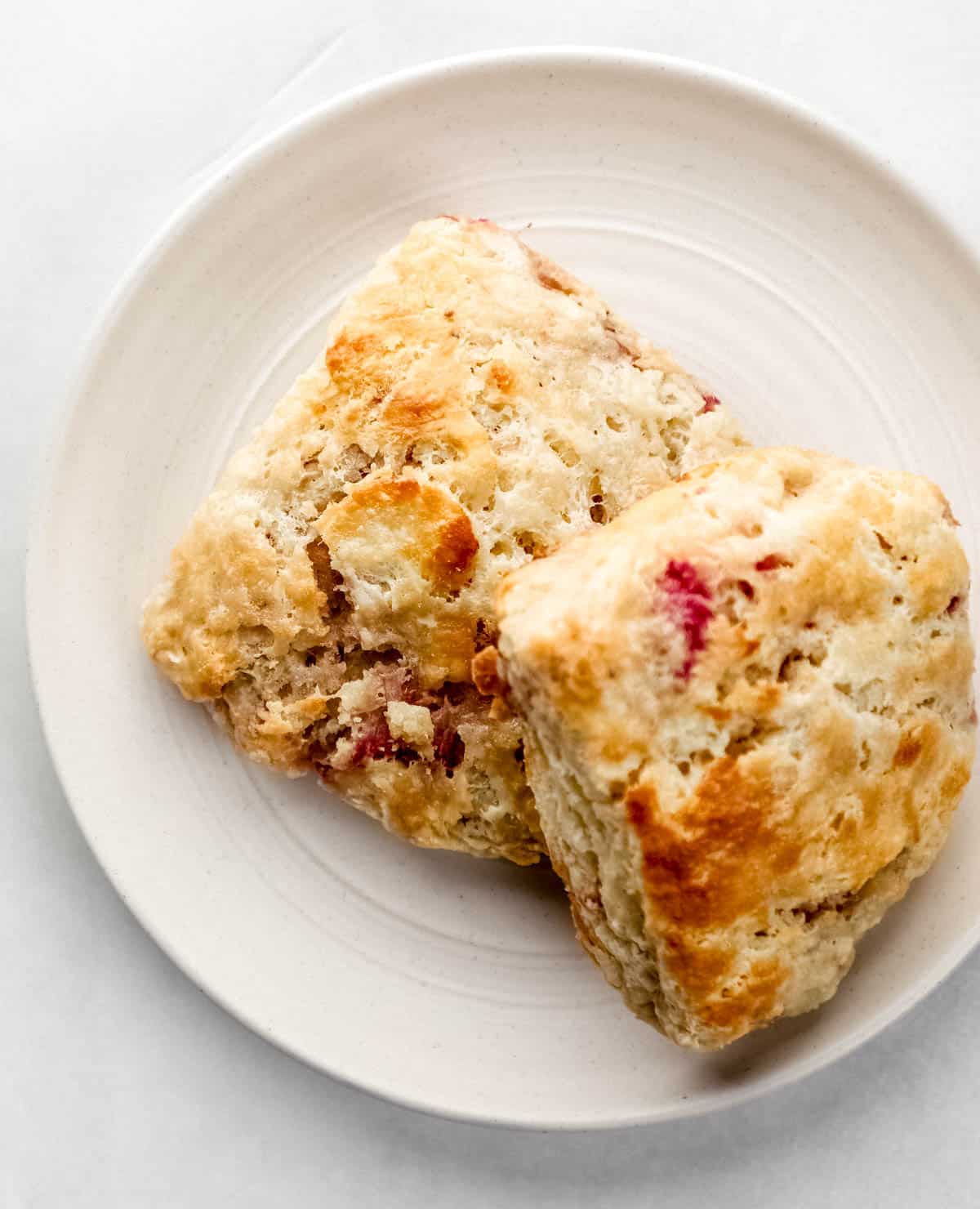 Overhead view of two biscuits on white plate on white surface. 