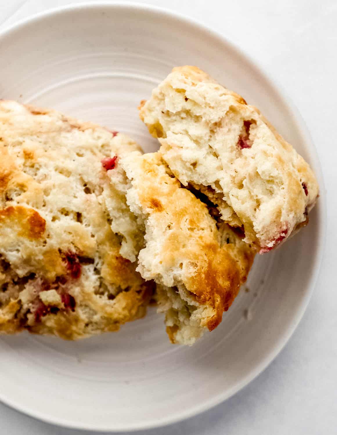 Two biscuits on white plate with one of the biscuits broke in half. 