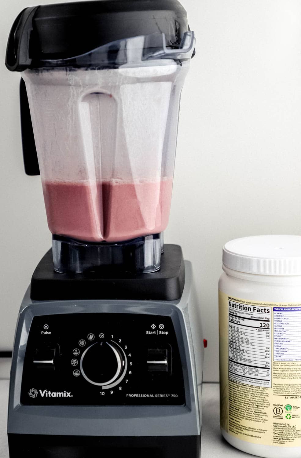 Close up front view of blender with smoothie ingredients blended in it by a protein container. 