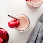 Overhead view of two smoothies in glasses by a bowl of frozen strawberries and cloth napkin.