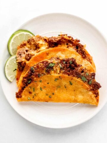 Overhead view of two tacos on a white plate with lime slices.