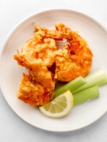 Three shrimp on white plate with celery sticks and lemon slices.