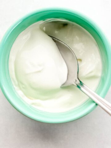 Overhead view of teal colored bowl with sour cream and spoon in it on grey surface.