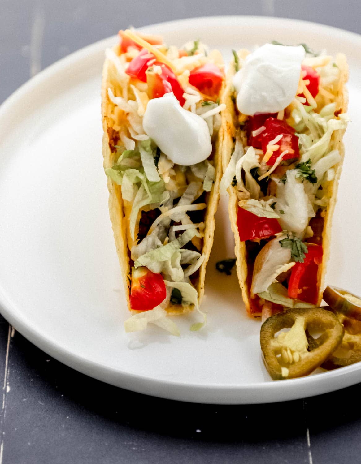 Close up front view of two tacos on white plate with jalapenos slices. 