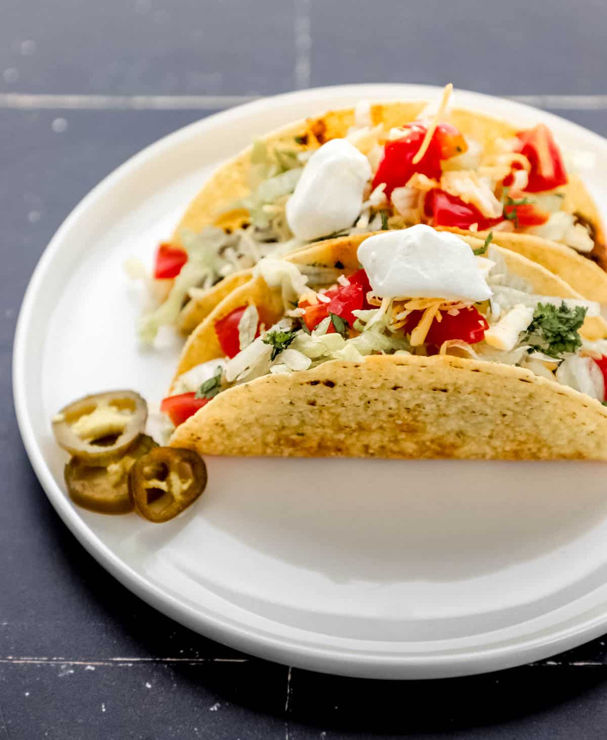 Close up side view of two tacos on white plate with jalapeno slices. 