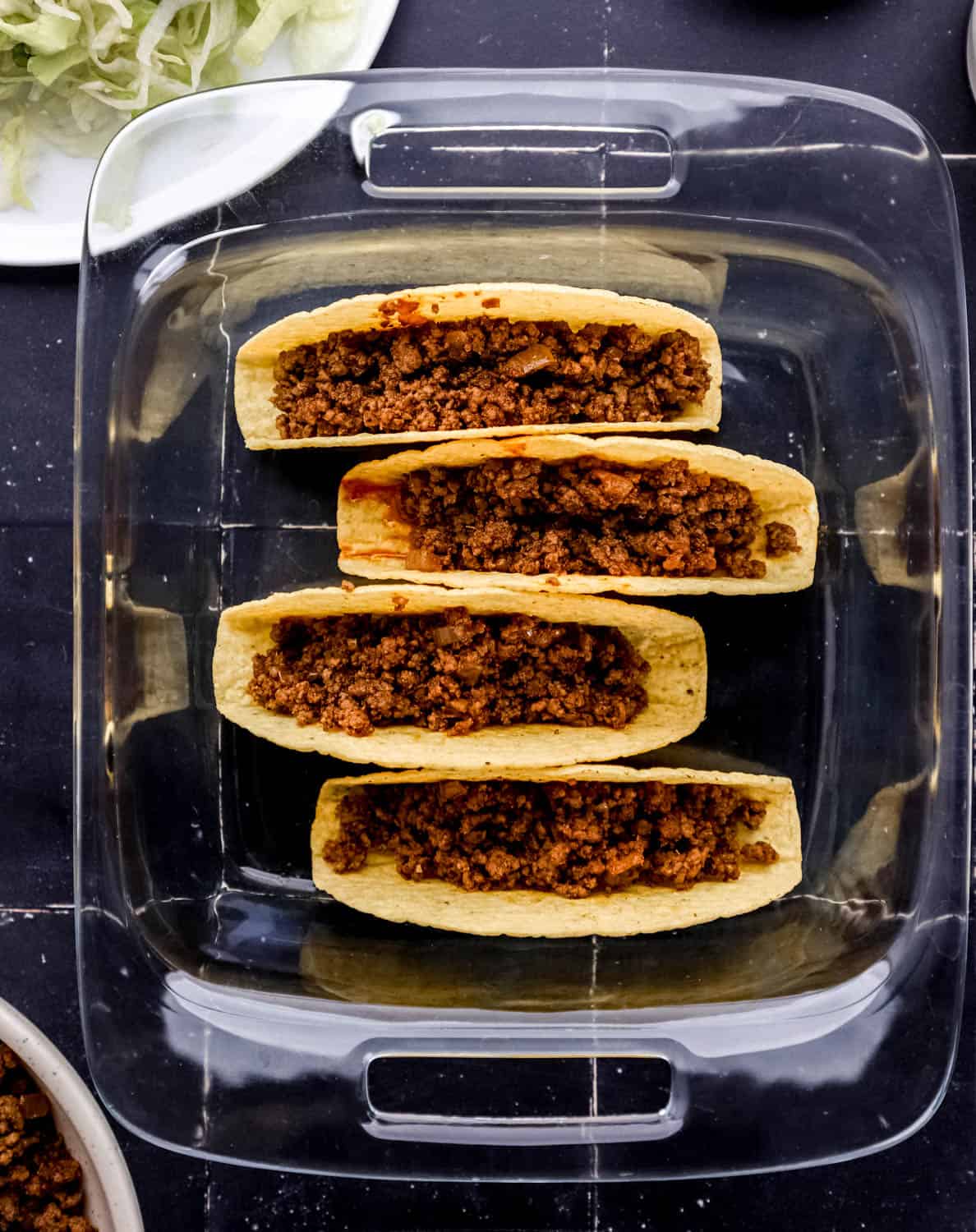 Beef mixture added to taco shells in glass baking dish. 