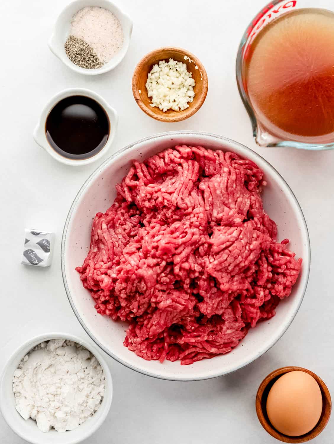 Overhead view of ingredients needed to make burger steaks in separate bowl on grey surface. 