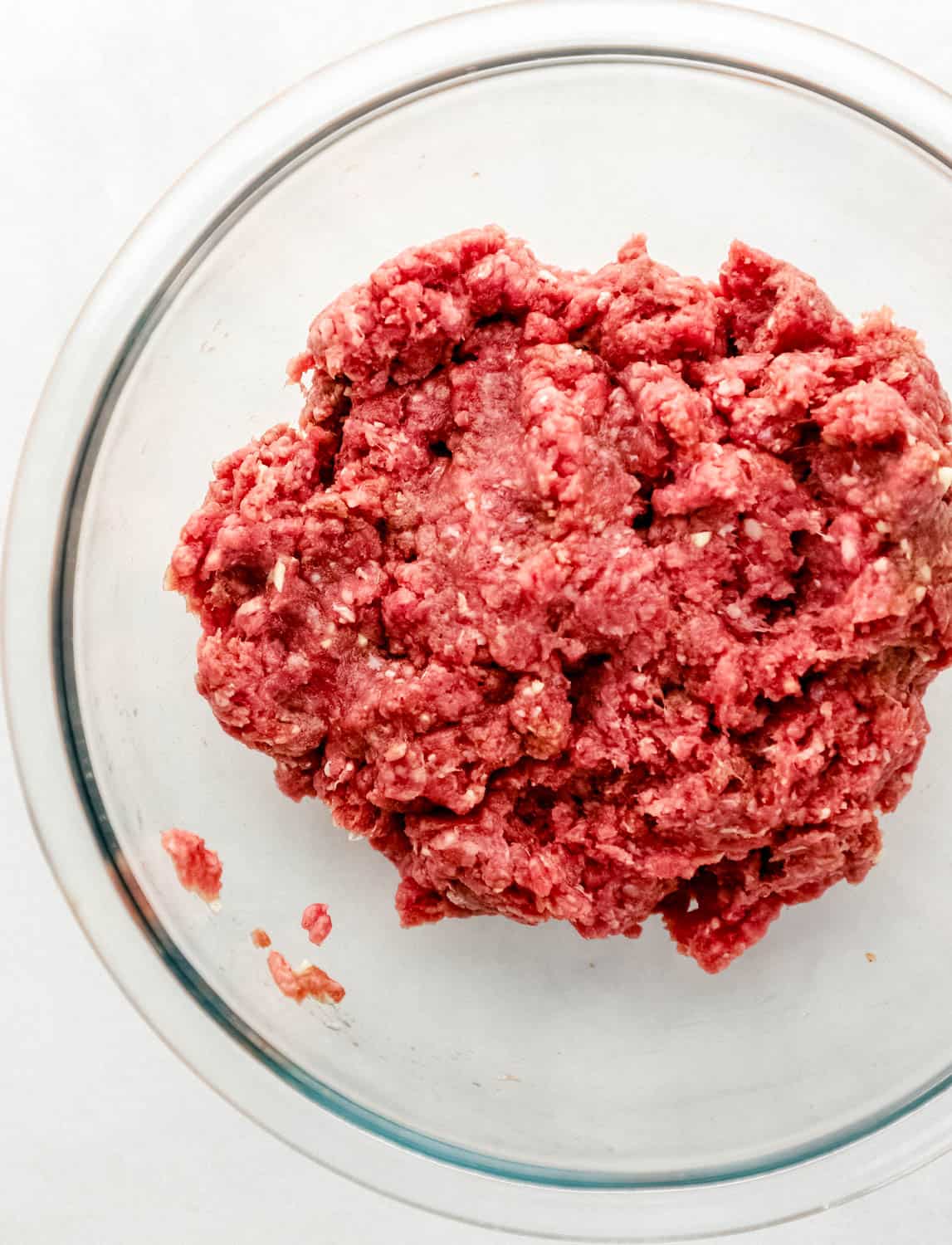 Meat mixture in large glass mixing bowl on grey surface. 