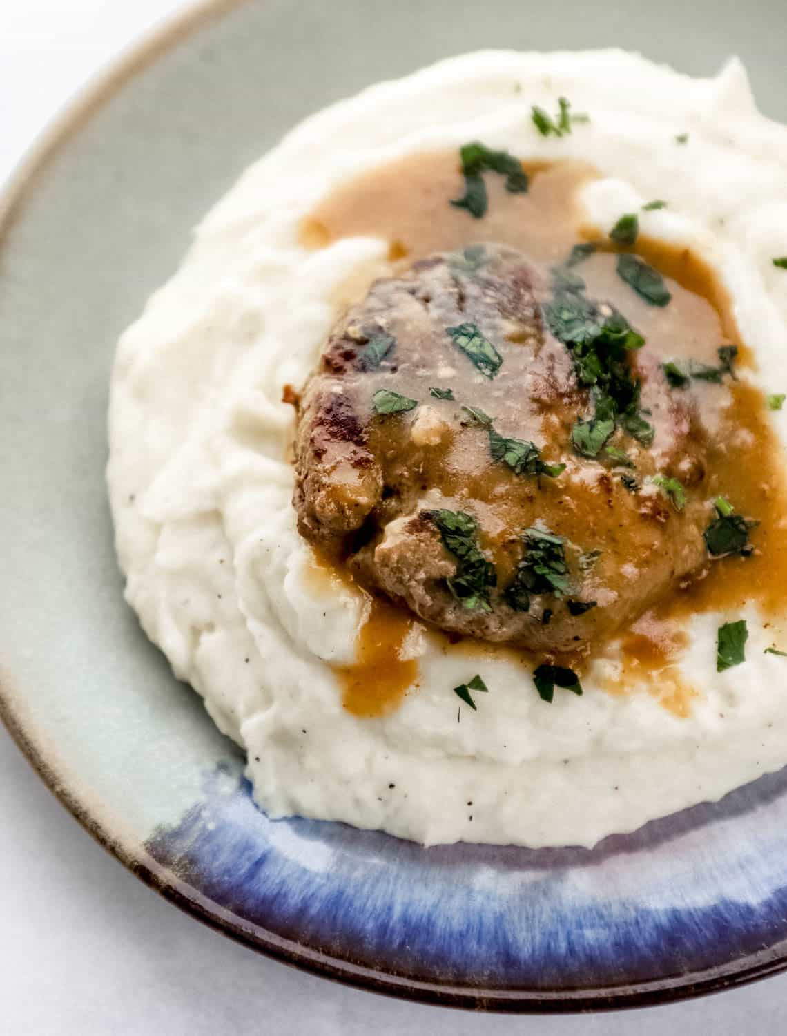 Overhead view of plate with mashed potatoes and hamburger steak on it topped with chopped parsley.