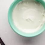 Overhead view of bowl of sour cream beside a spoon.
