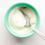 Overhead view of sour cream in teal colored bowl with spoon in it.