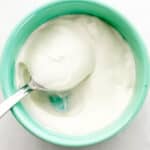 Close up overhead view of bowl of sour cream with spoon in it on grey surface.