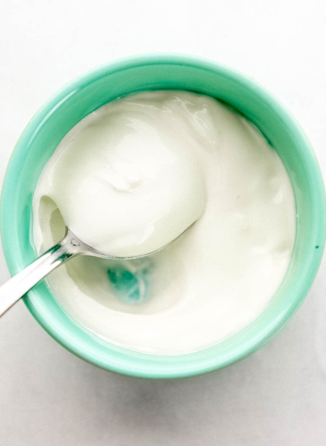 Close up overhead view of sour cream in teal bowl with spoon in it on grey surface. 