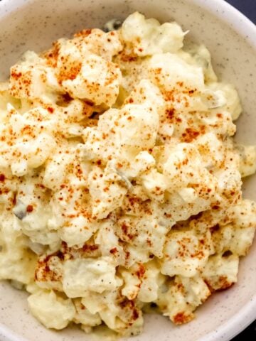Close up overhead view of finished potato salad topped with paprika in white bowl.