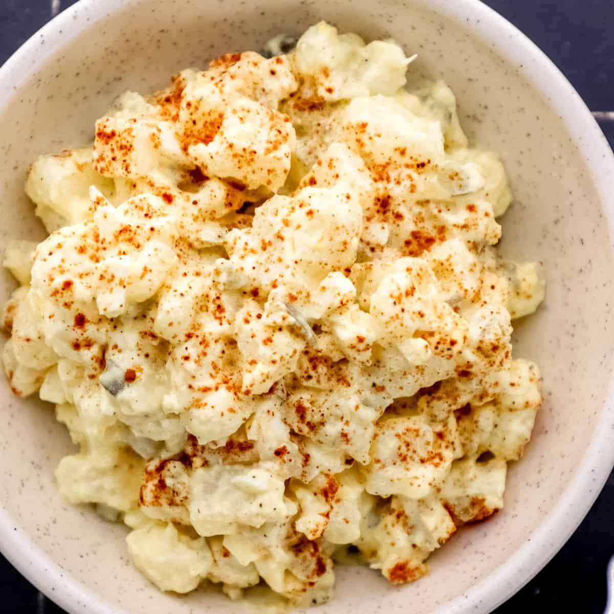 Close up overhead view of finished potato salad topped with paprika in white bowl.