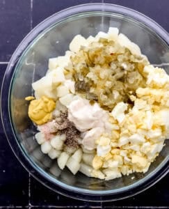Overhead view of potato salad ingredients in glass mixing bowl.