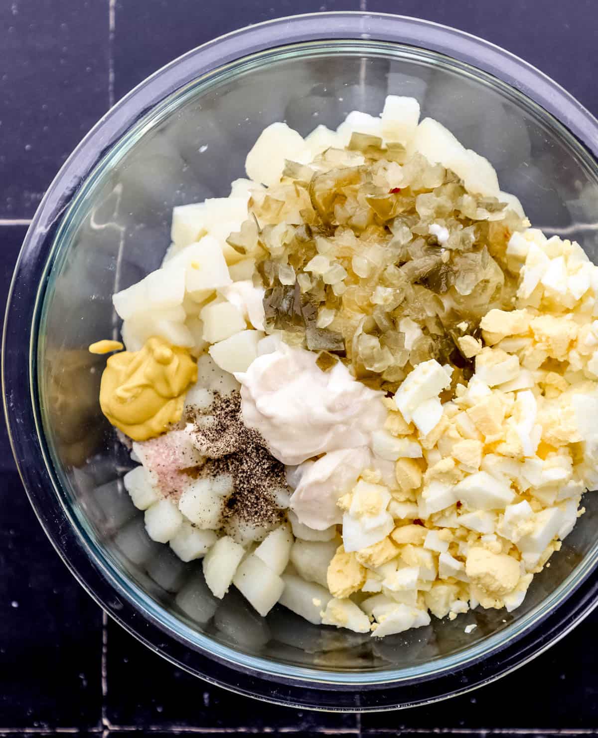 Ingredients to make potato salad added to large glass mixing bowl. 