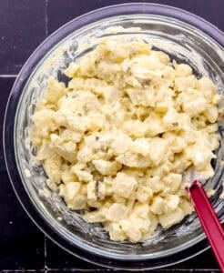 Ingredients for potato salad combined in mixing bowl with rubber spatula.