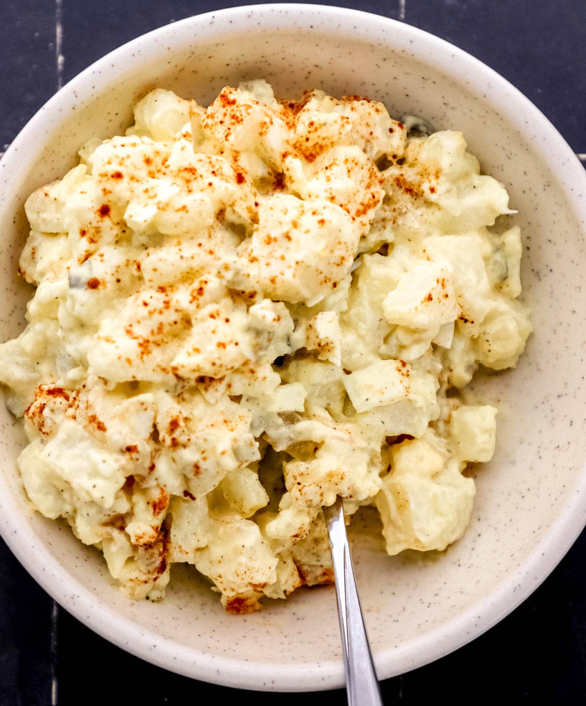 Potato salad in white bowl with fork in it. 