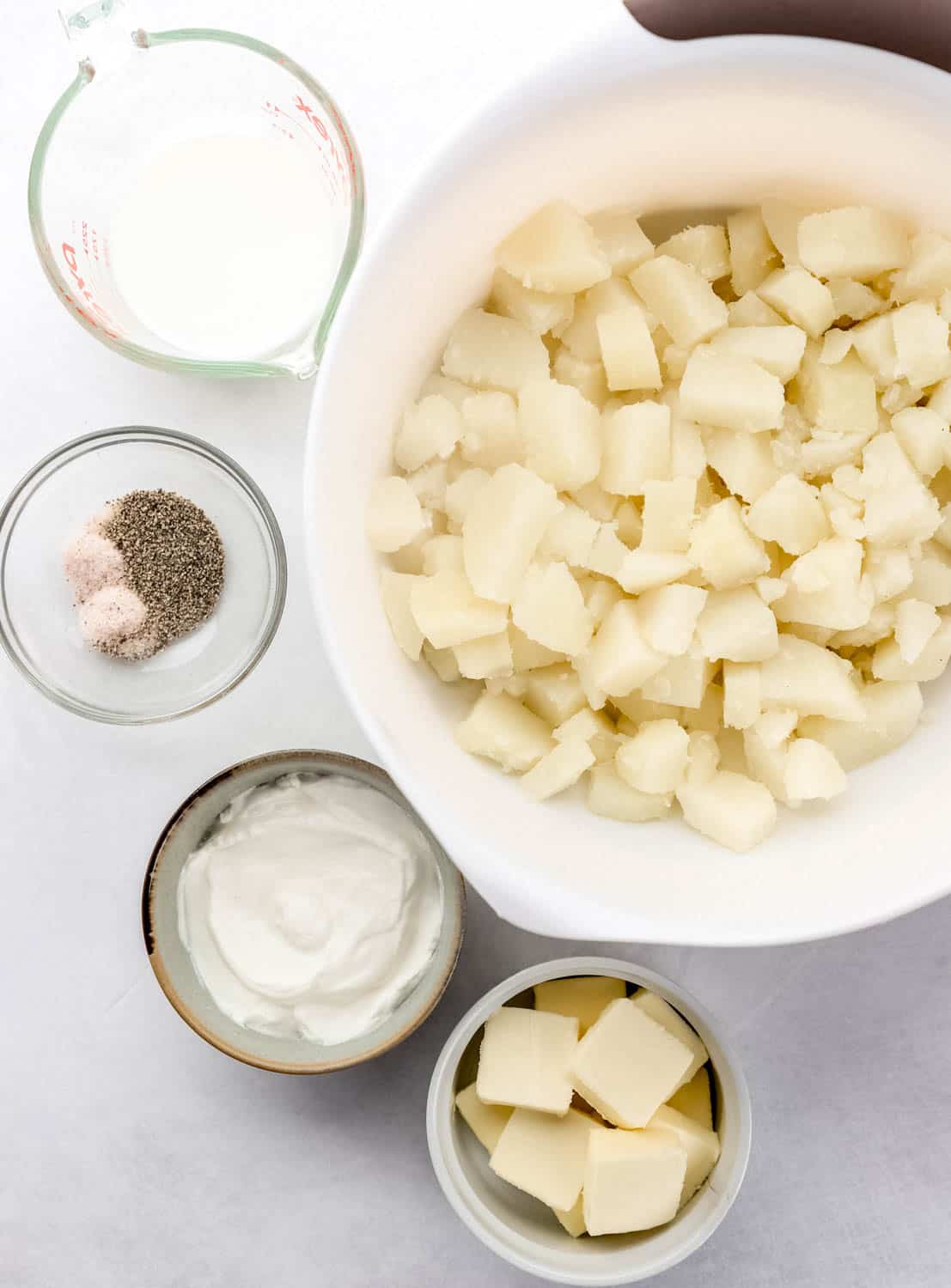 Overhead view of ingredients needed to make mashed potatoes in separate bowls on grey surface. 