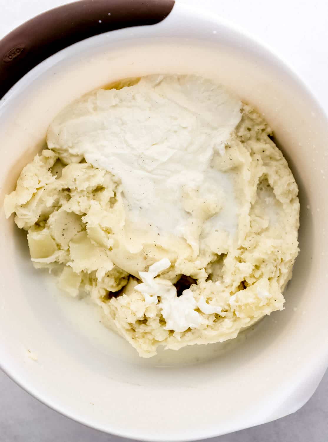 Milk and sour cream added to other mashed potato ingredients in large white mixing bowl. 