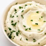Close up front view of potatoes in white bowl on grey surface.