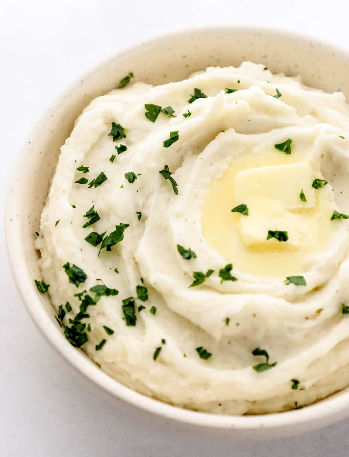 Close up front view of mashed potatoes in white bowl on grey surface. 