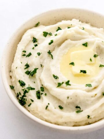 Close up front view of potatoes in white bowl on grey surface.