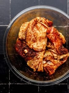 Overhead view of seasoned chicken in glass mixing bowl.